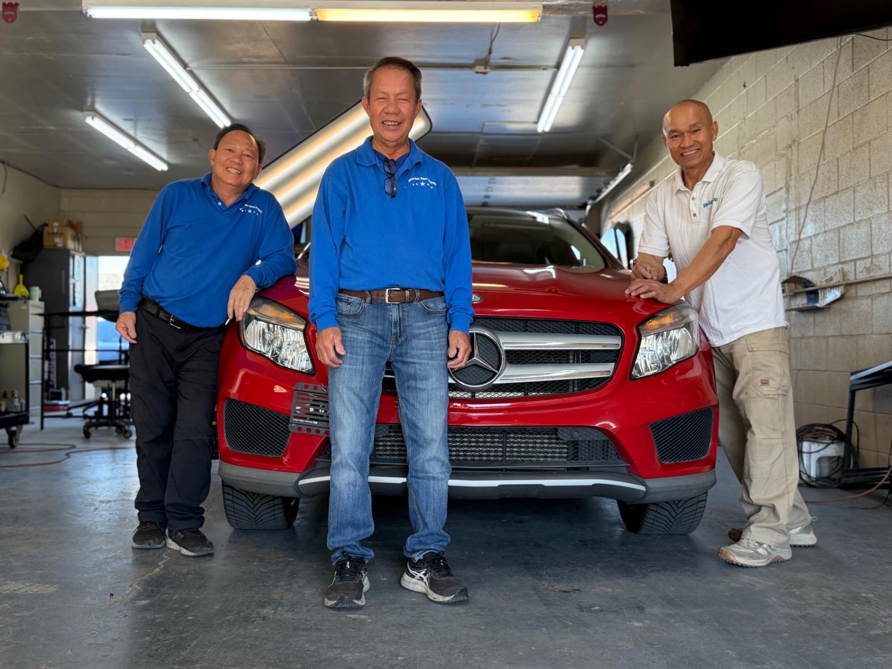 Three Blue Star Dent Repair technicians standing in front of a red SUV inside the Arvada shop