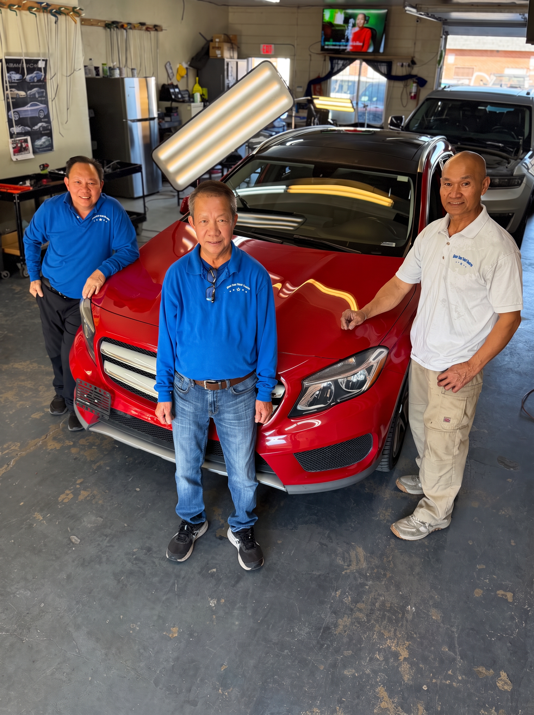 Thongsy and the Blue Star team beside a red Mercedes in the Arvada shop, with a paintless dent repair light board