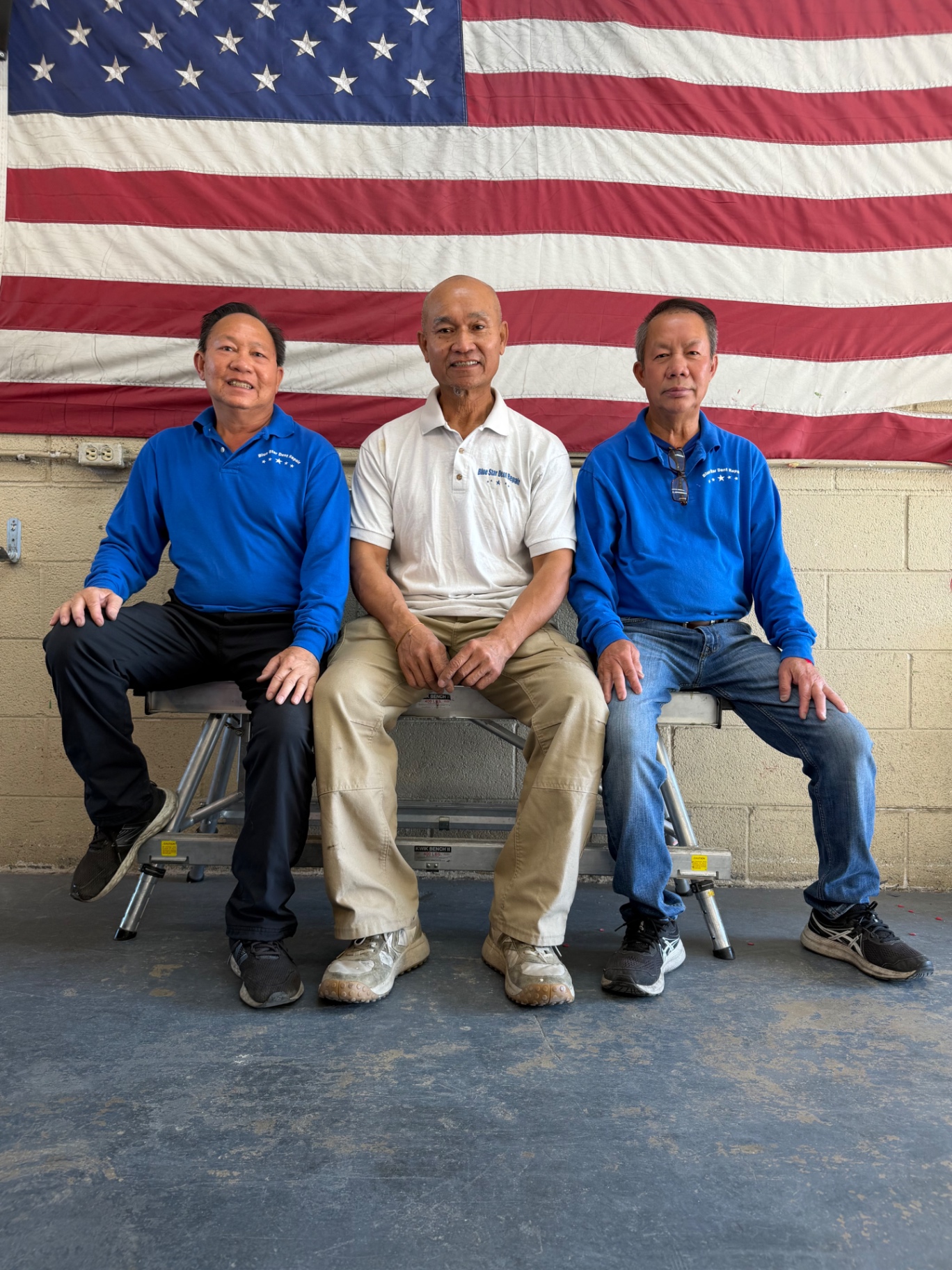 Three Blue Star Dent Repair technicians seated together at the shop bench